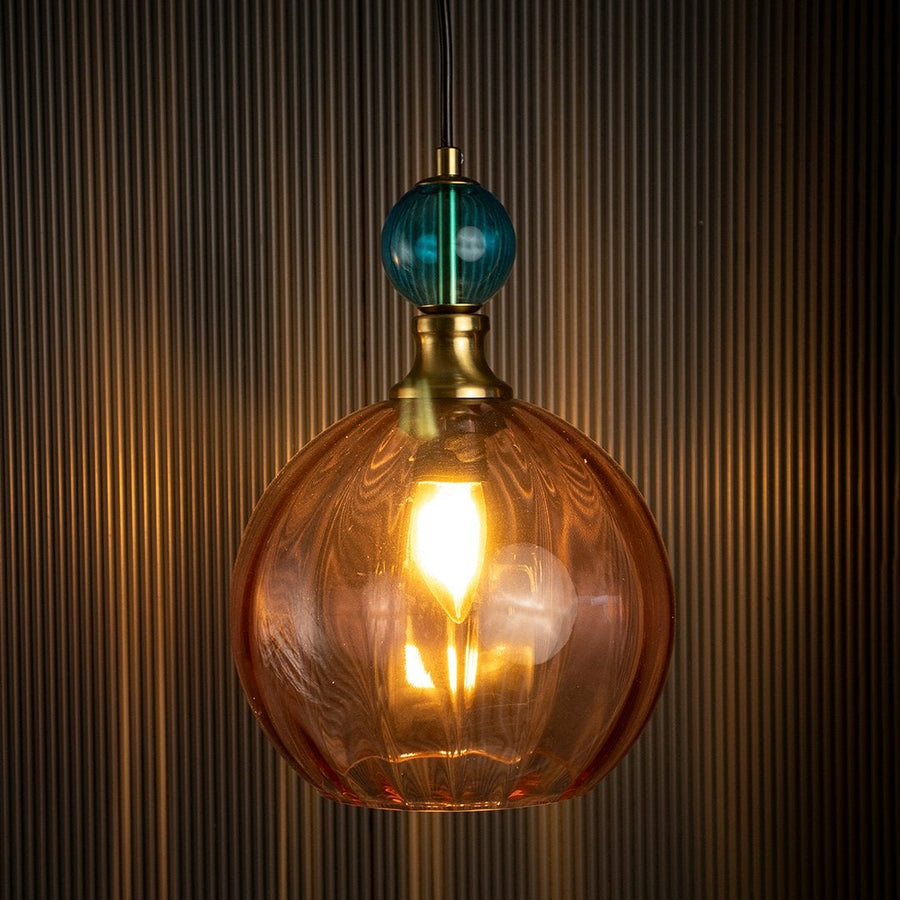 Glowing glass pendant light with amber globe and teal top element highlighting vintage-inspired craftsmanship.