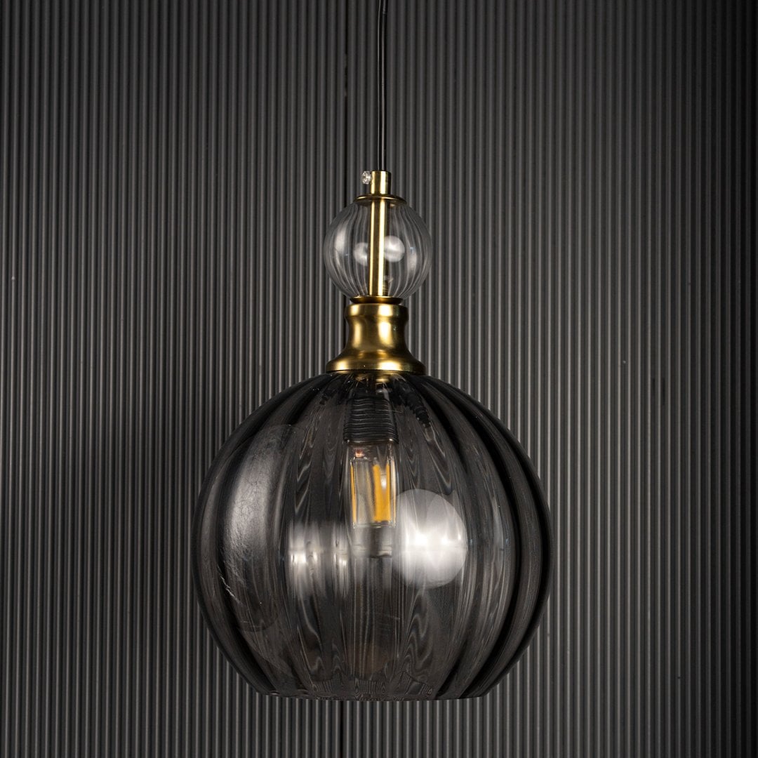 Smoky glass pendant lamp turned off against black background with gold metal holder and clear glass top accent designed for modern interiors.