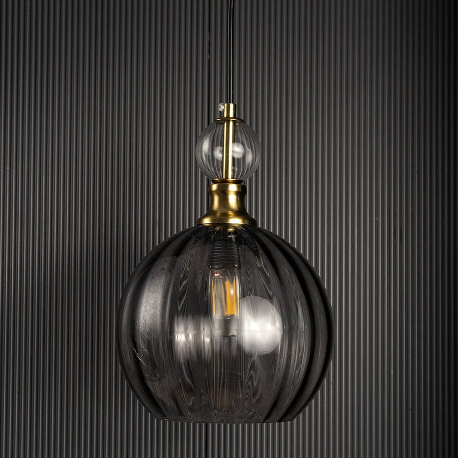 Smoky glass pendant lamp turned off against black background with gold metal holder and clear glass top accent designed for modern interiors.