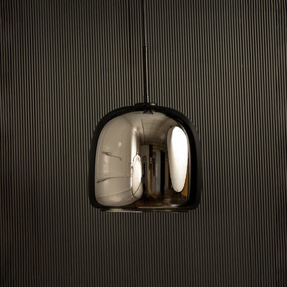 Metallic pendant light with a smooth rounded reflective shade glowing softly against a dark backdrop adding a sleek modern lighting highlight to the surrounding interior.