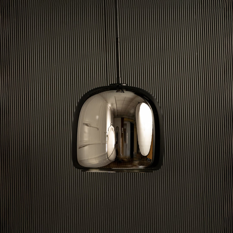 Metallic pendant light with a smooth rounded reflective shade glowing softly against a dark backdrop adding a sleek modern lighting highlight to the surrounding interior.
