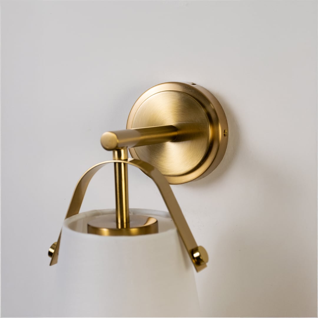 Closeup of gold metal wall light with white fabric shade showing fine detailing and elegant finish for refined modern indoor lighting.