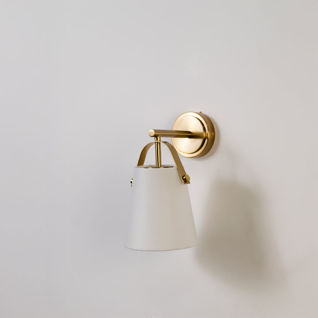 Gold metal wall light with white fabric shade displayed on a white background with light off showing its sleek modern shape and finish.