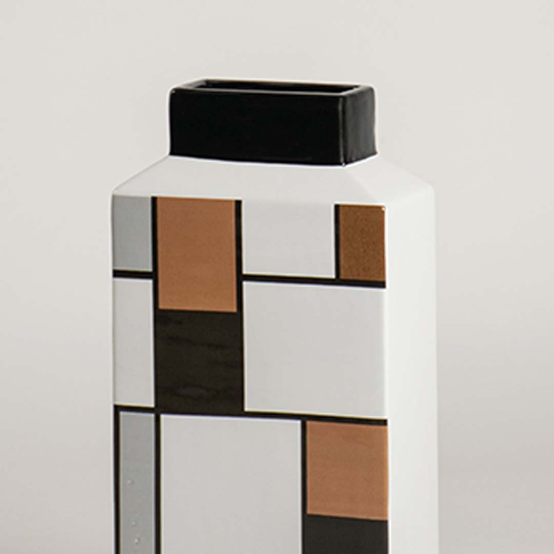 Closeup view of the geometric ceramic vase showing its bold black white and bronze block detailing with a smooth finish.
