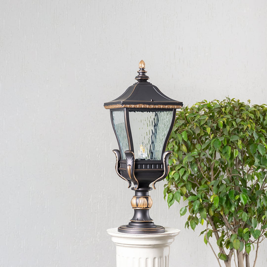 Stylish black and gold outdoor pillar light with clear glass shade displayed on decorative column shown in switched off mode.