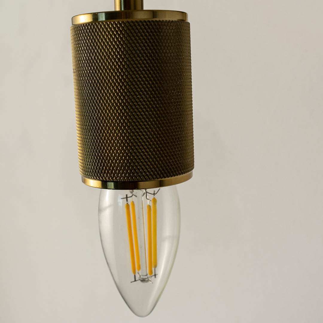 Closeup of textured gold metal wall light with clear glass bulb for modern bedroom and luxury hallway decor spaces.