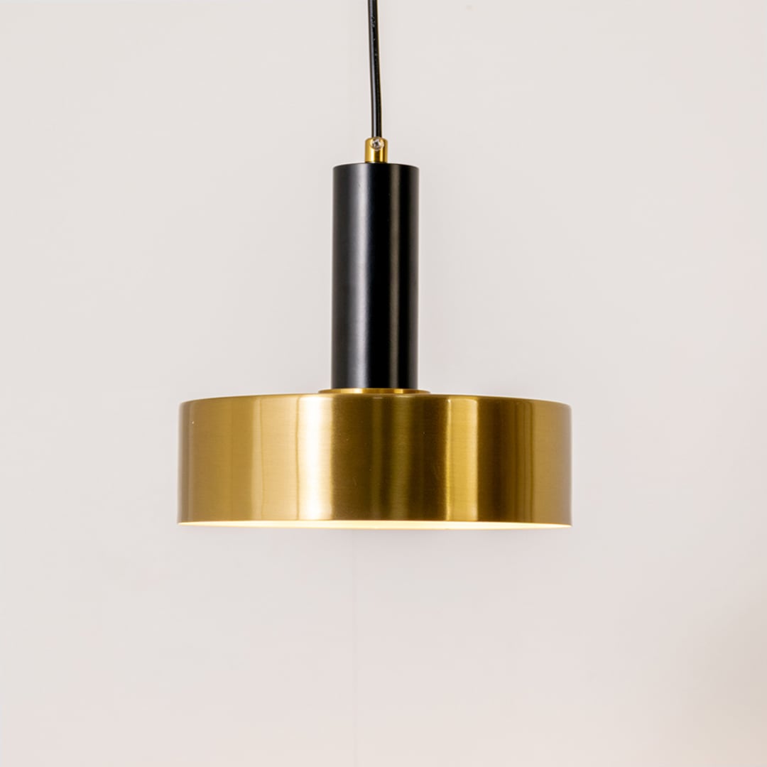 Gold and black metal pendant light on white background with light on displaying a warm downward glow and a sleek modern circular design.