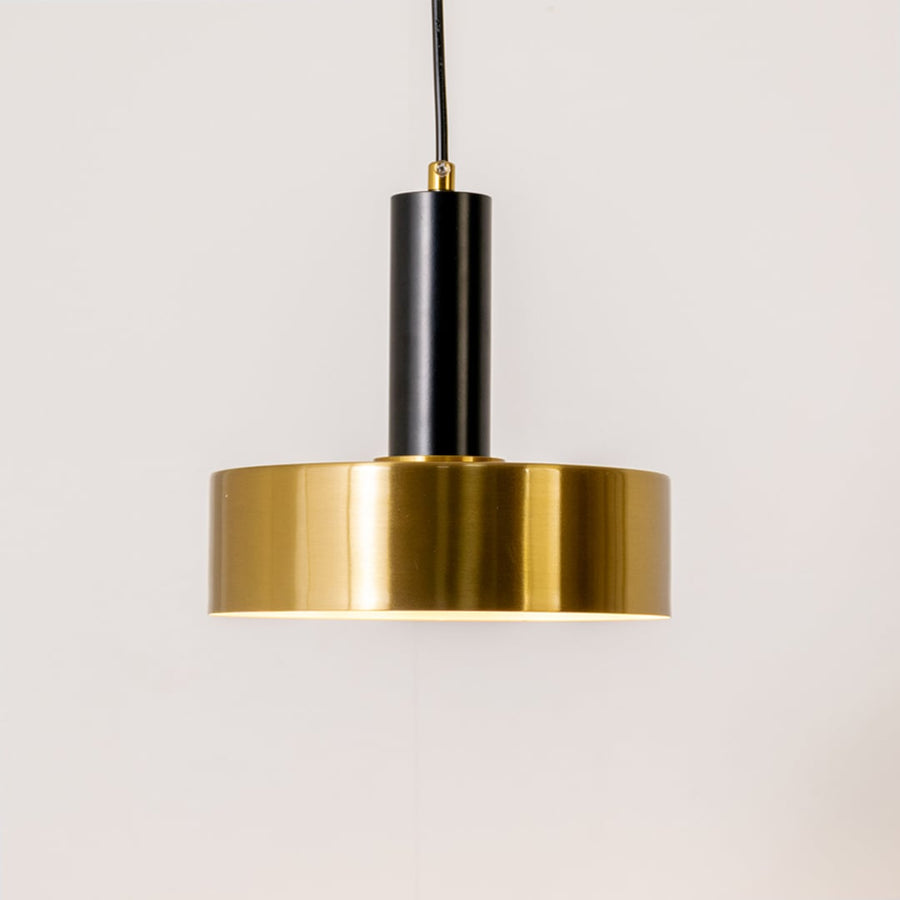 Gold and black metal pendant light on white background with light on displaying a warm downward glow and a sleek modern circular design.