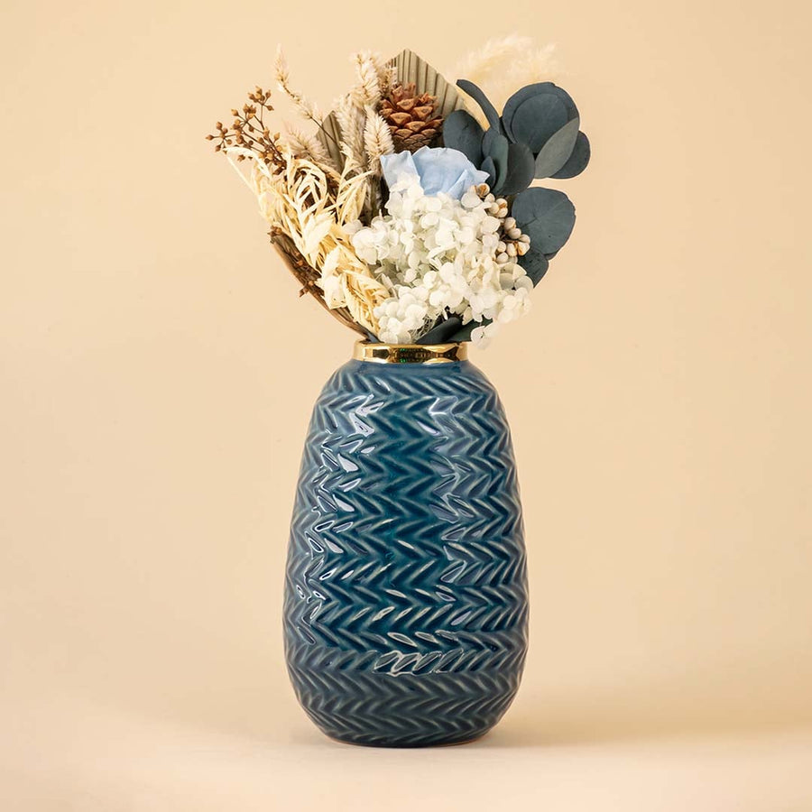 Modern blue ceramic vase with embossed zigzag design and gold top placed near a classic gold mirror in a cozy interior.