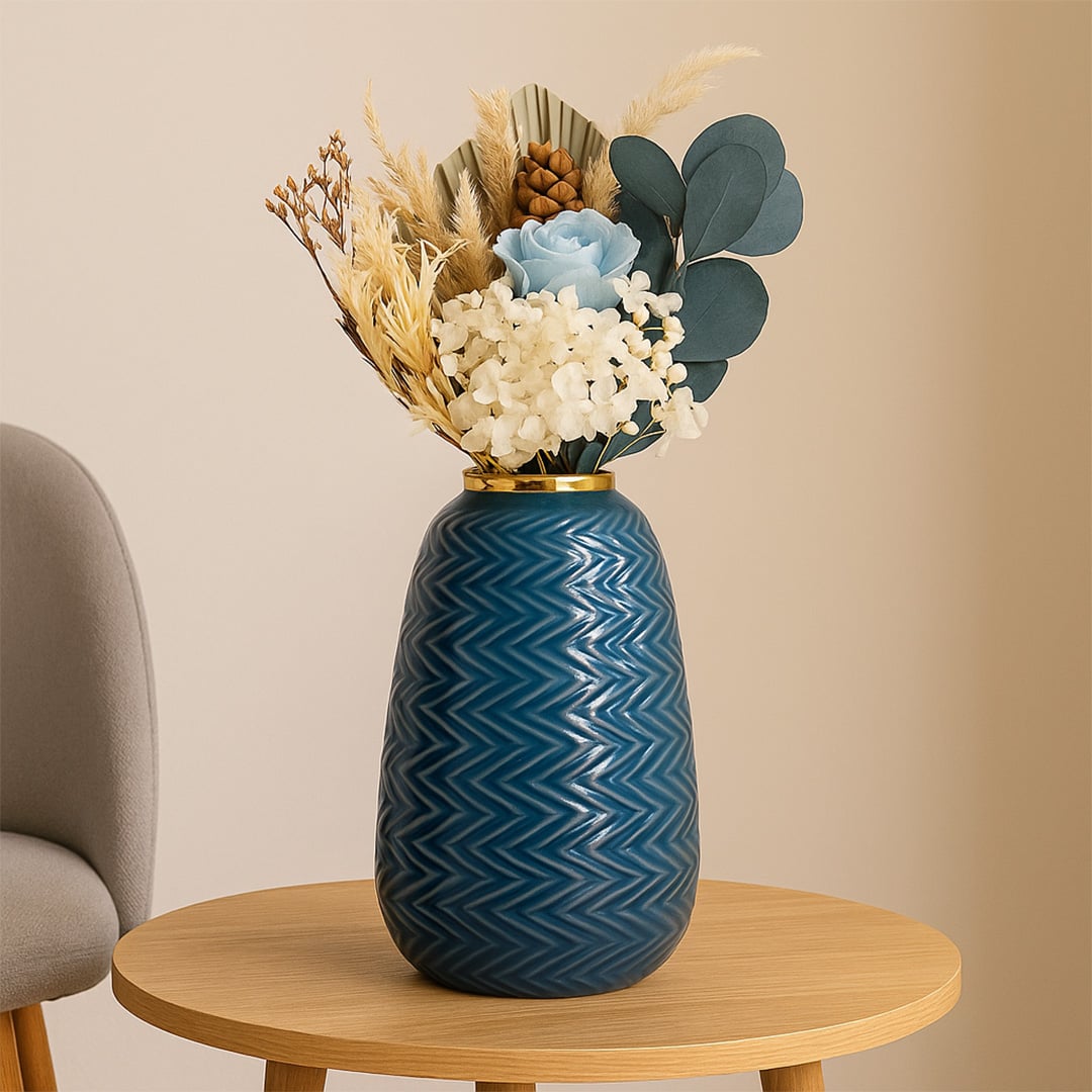 Modern blue ceramic vase with embossed zigzag design and gold top placed near a classic gold mirror in a cozy interior.