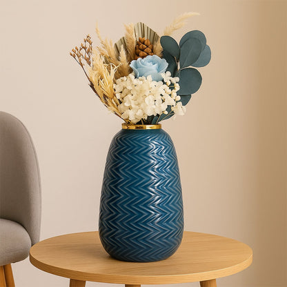 Modern blue ceramic vase with embossed zigzag design and gold top placed near a classic gold mirror in a cozy interior.