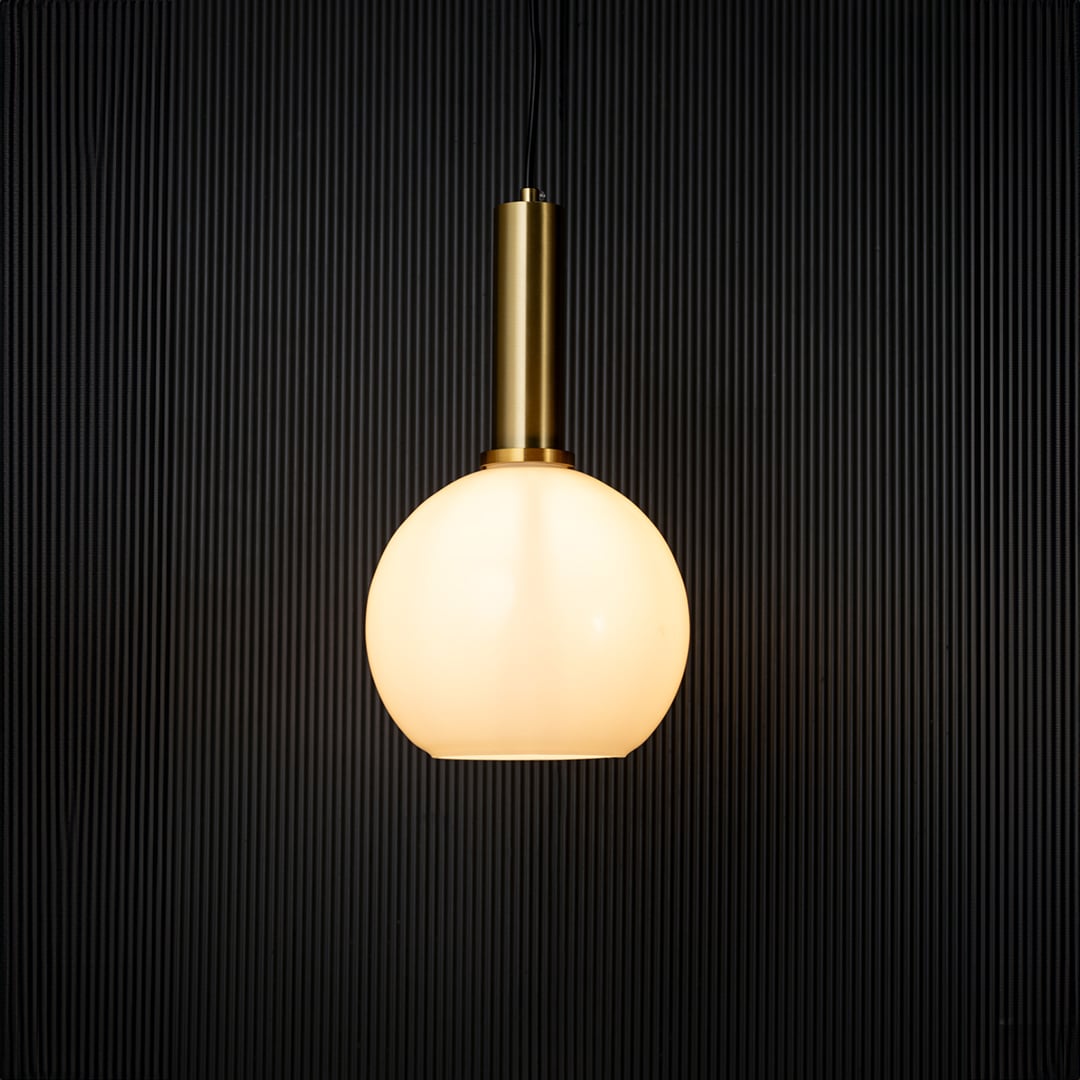 Stylish globe pendant light turned on with warm glow creating modern ceiling decor effect on black background.