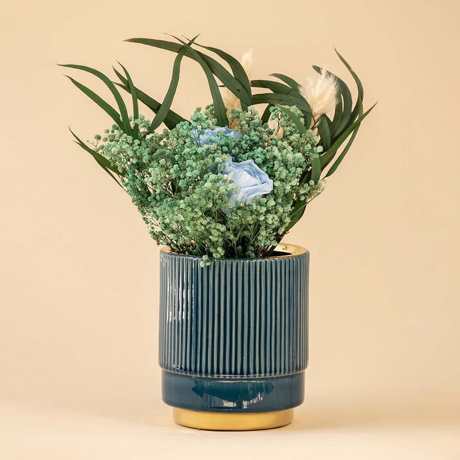 Elegant blue ceramic vase with ribbed texture and metallic gold bottom displayed with delicate flowers.