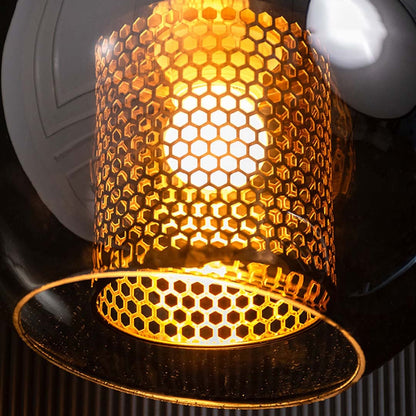 Closeup off smoky globe pendant light with brass stem shown turned off on a black background with a glossy reflective surface.