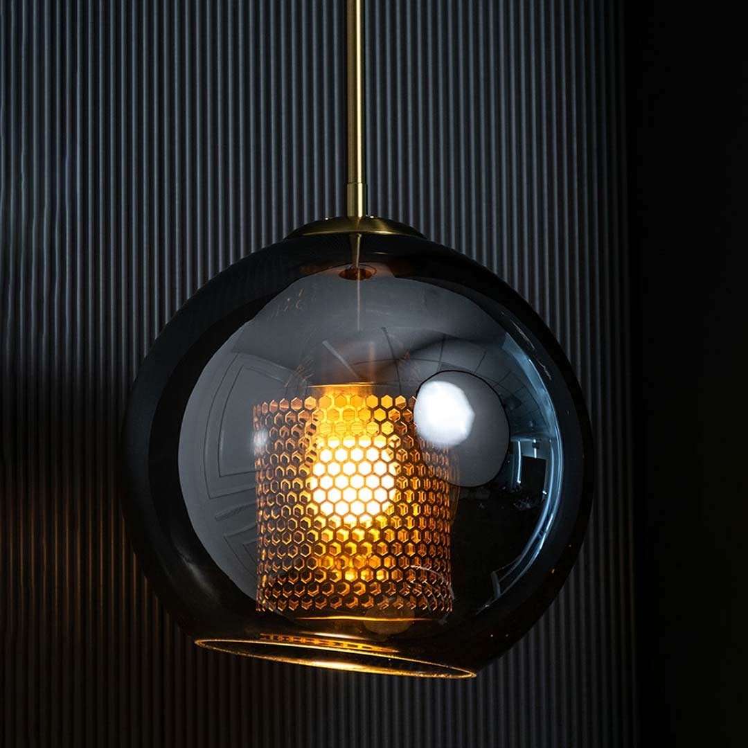 Pendant light with smoky reflective glass globe and glowing inner mesh diffuser lit against a dark black background.
