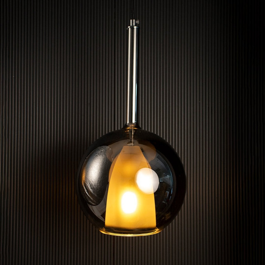 Modern glass pendant light with warm glow and metal suspension hanging in contemporary interior setting for dining living spaces.