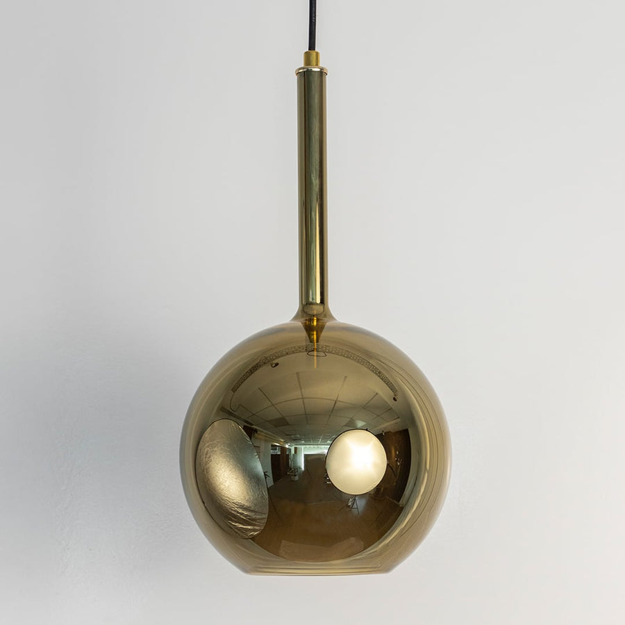 Amber pendant light off white background featuring round glass shade with warm golden tone and sleek black cord.