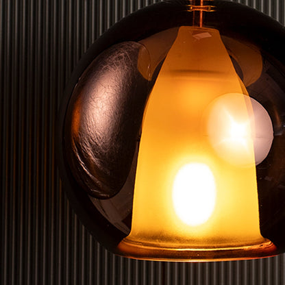 Closeup of amber pendant light showing smooth glass surface and soft diffused glow from warm LED bulb.