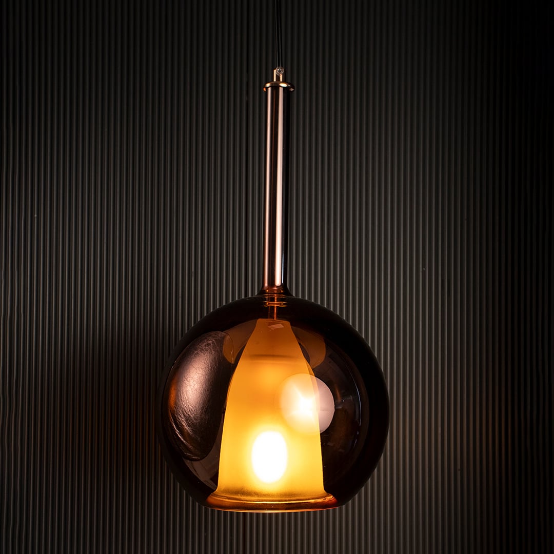 Amber pendant light glowing gently against dark background emphasizing its warm amber glass finish.
