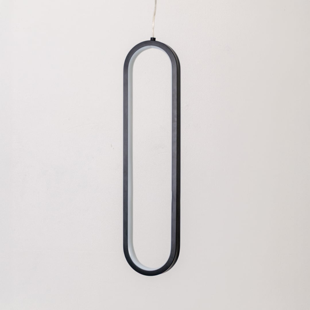 Modern metal elongated loop hanging light in black and white shown switched off on white background for minimal wall decor.
