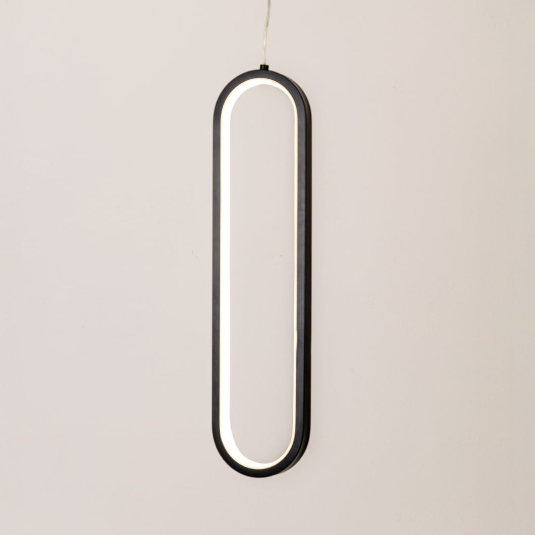 Modern metal elongated loop hanging light in black and white glowing softly on white background for stylish wall decor.