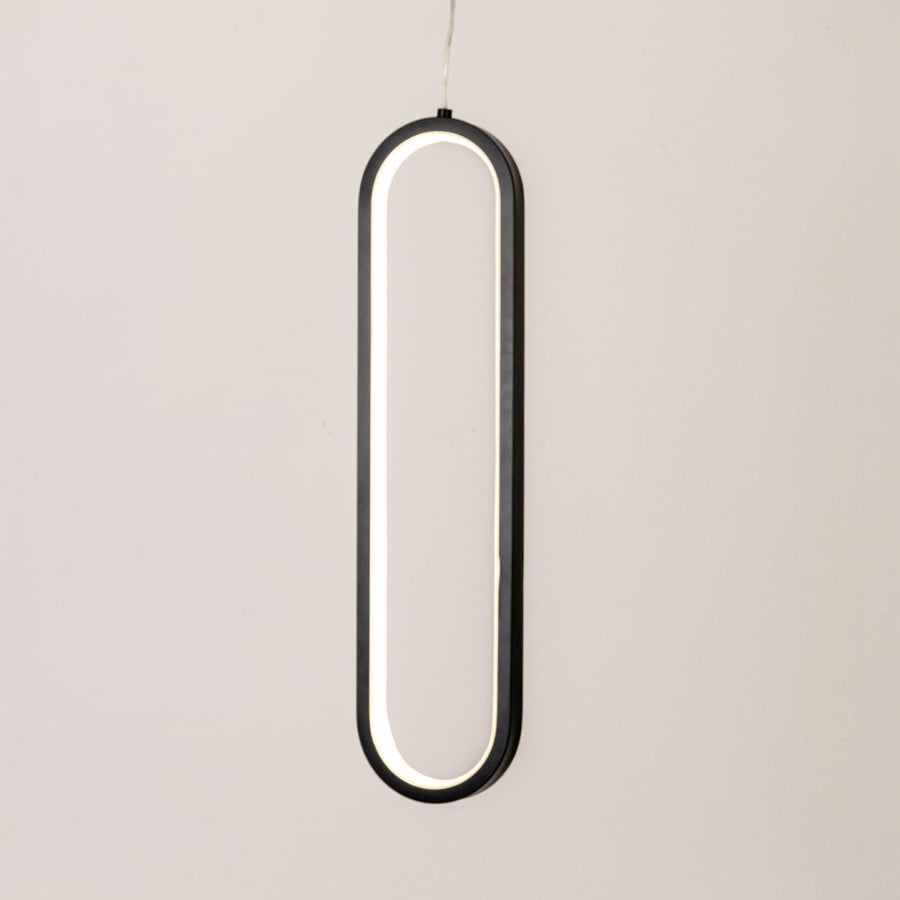 Modern metal elongated loop hanging light in black and white glowing softly on white background for stylish wall decor.