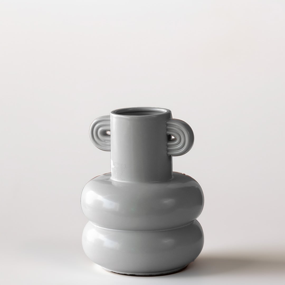 Grey sculptural vase placed on a marble surface with a warm brown backdrop creating a soft lifestyle scene.
