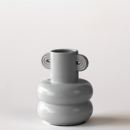 Grey sculptural vase placed on a marble surface with a warm brown backdrop creating a soft lifestyle scene.