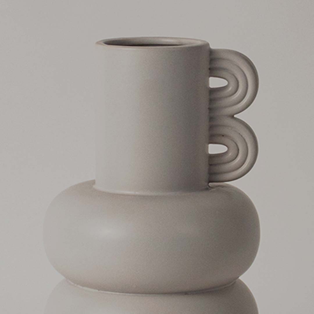 A closeup view of the sculptural neutral vase showing its smooth rounded body layered design and unique loop side detail.