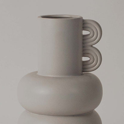A closeup view of the sculptural neutral vase showing its smooth rounded body layered design and unique loop side detail.