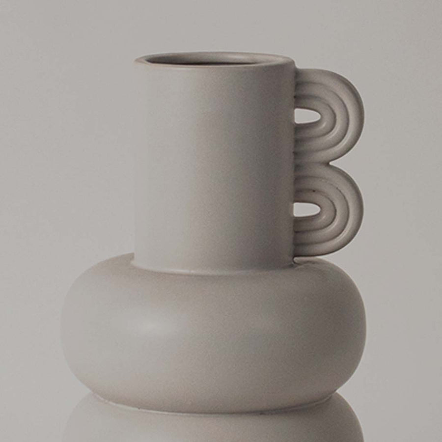 A closeup view of the sculptural neutral vase showing its smooth rounded body layered design and unique loop side detail.