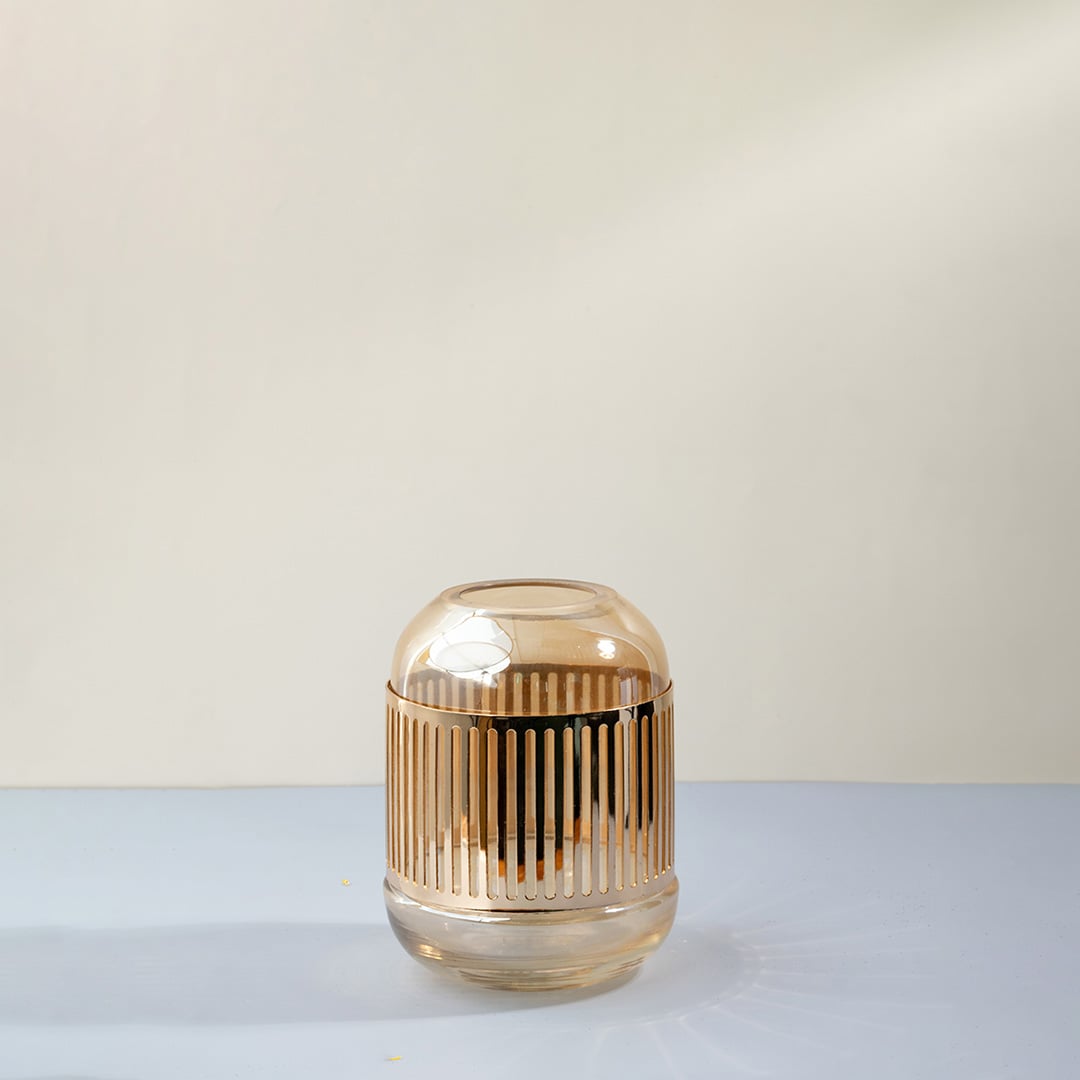 Decorative glass candle holder with vertical ribbed design and warm amber finish displayed on white background for modern table decor.
