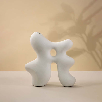 Abstract white sculptural ceramic vase with smooth organic structure and hollow detailing for visual interest against white background.