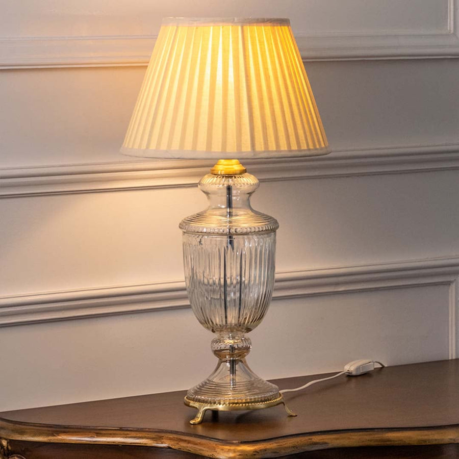 Crystal glass table lamp with warm illuminated pleated shade creating inviting ambient lighting for luxury interiors.