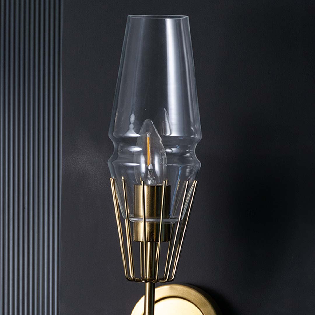 Closeup of sleek unlit wall lamp with brass cage detail and clear glass shade shown on black background showcasing premium metal finish and quality.