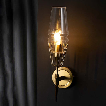 Glowing gold wall light fixture with glass shade set against dark black background emphasizing dramatic ambiance and torch silhouette design.