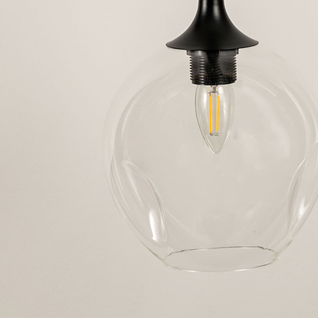 Detailed closeup of clear glass pendant light with visible filament bulb and black ceiling fixture.