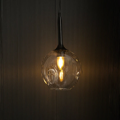 Clear glass pendant light with black fixture glowing warmly against black background.
