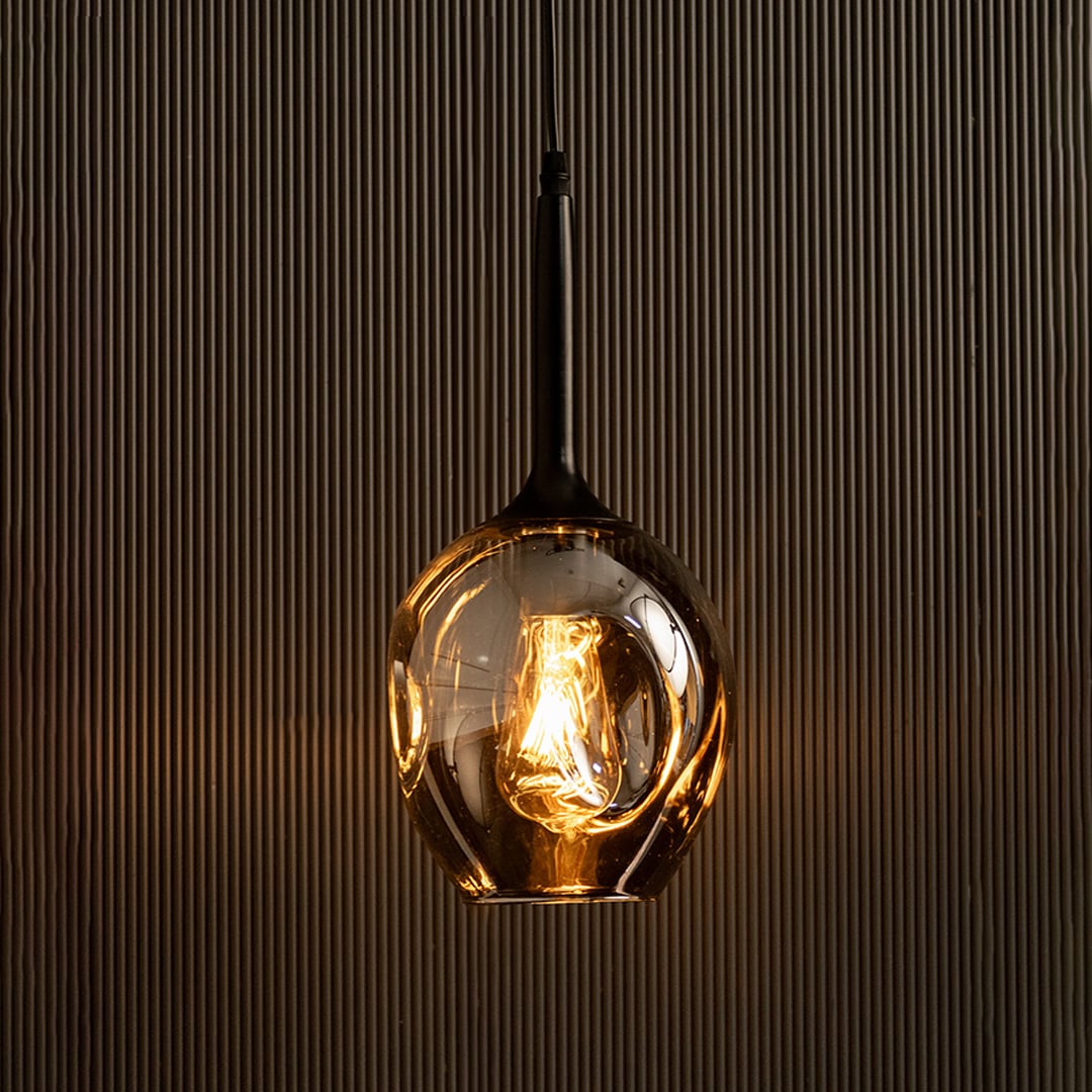 Illuminated chrome glass pendant light glowing against black background for luxury decor.
