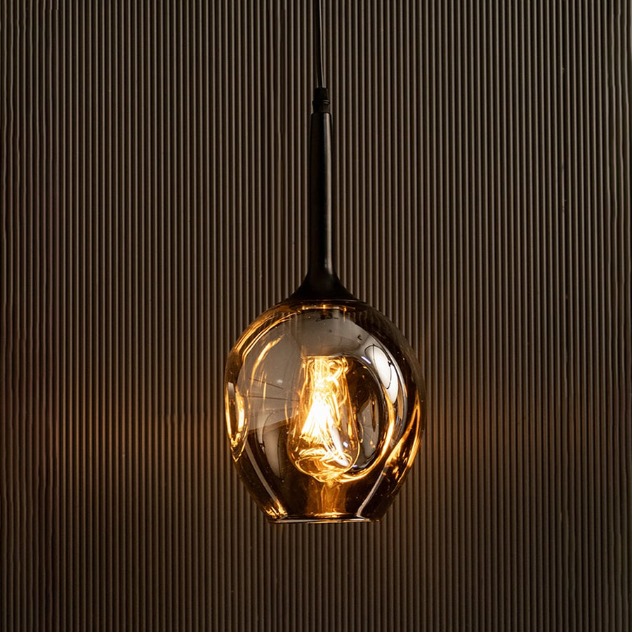 Illuminated chrome glass pendant light glowing against black background for luxury decor.