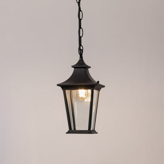 Black metal hanging lantern with clear glass glowing softly on a white background for outdoor home lighting.