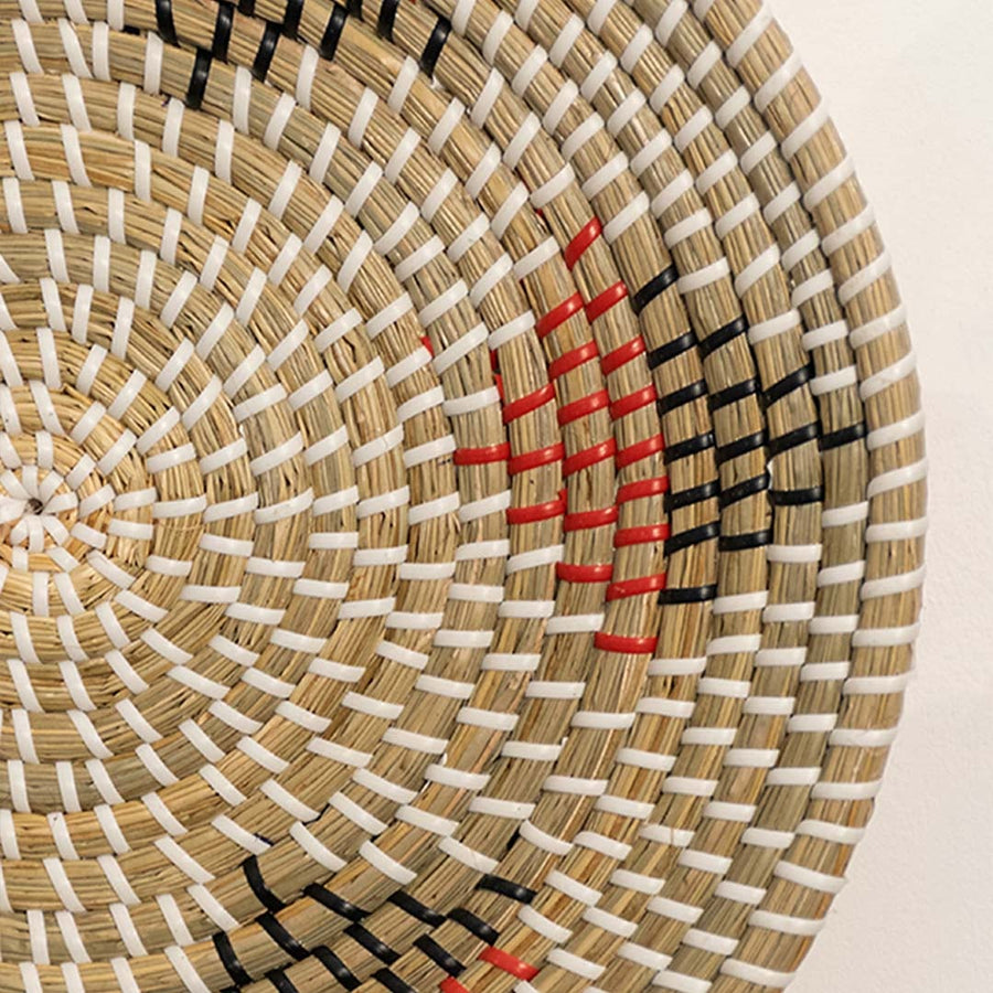 Closeup of handwoven wall basket showing natural fiber texture with beige black and red detailing highlighting artisan craftsmanship.