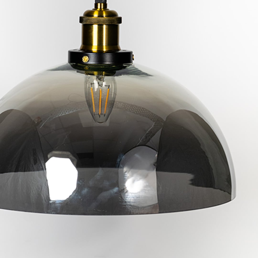 Closeup of smokey glass dome pendant light with brass and black fitting designed for elegant home interiors.
