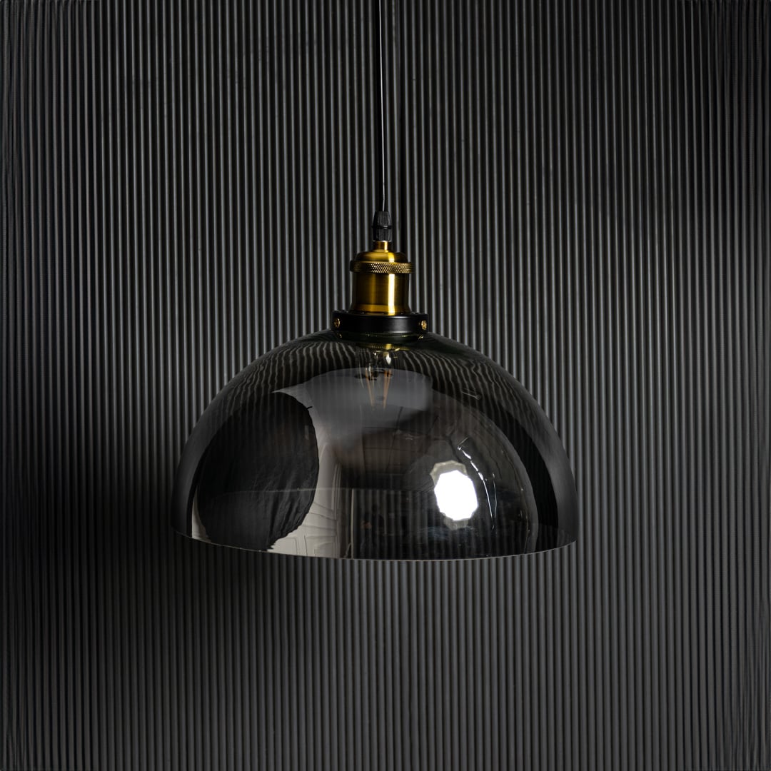 Light off black background presents smoked glass pendant light unlit focusing on dark tinted glass and brass detailing.