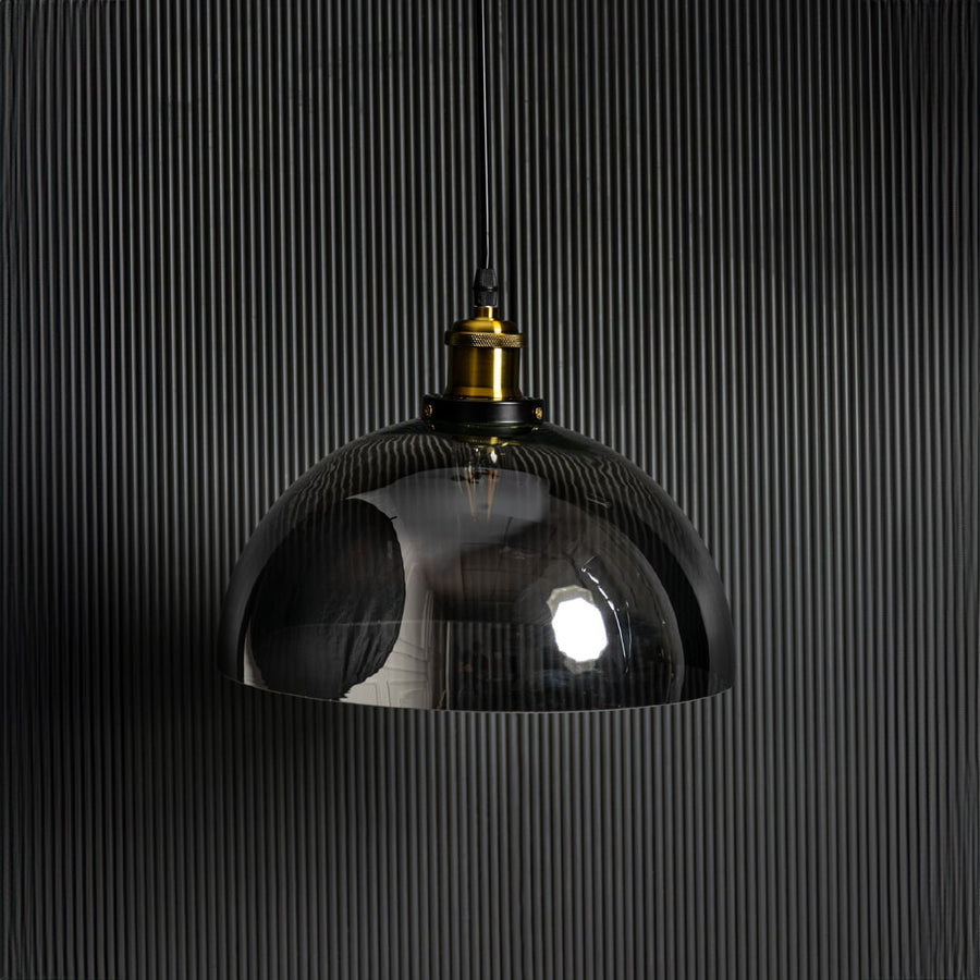 Light off black background presents smoked glass pendant light unlit focusing on dark tinted glass and brass detailing.