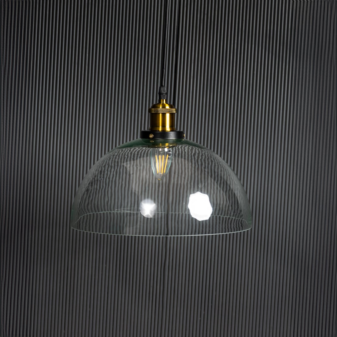 Clear glass dome pendant light with bulb off on black background featuring brass and black metal fitting design.