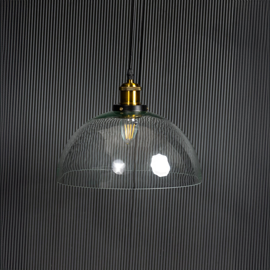 Clear glass dome pendant light with bulb off on black background featuring brass and black metal fitting design.