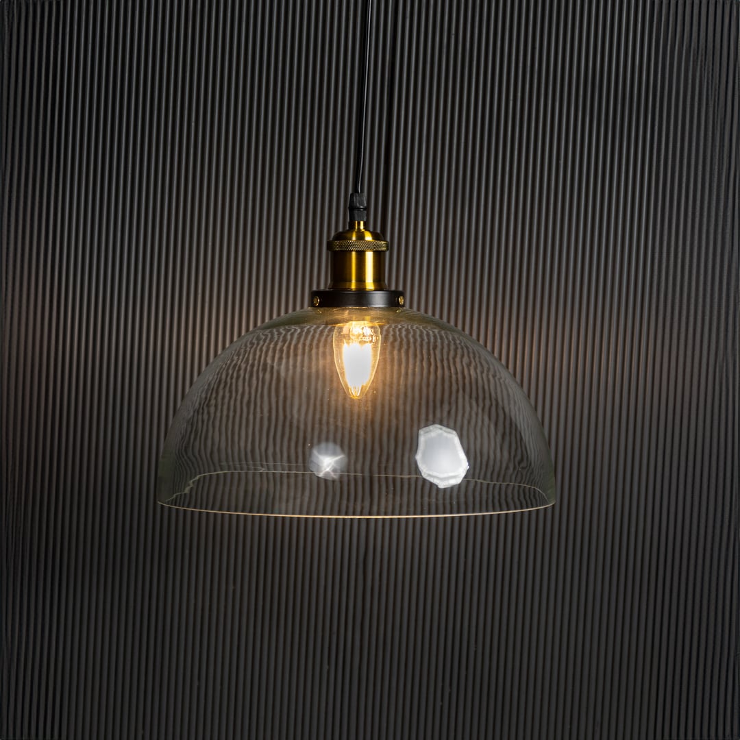 Clear glass dome pendant light glowing on black background with brass top and black fitting for stylish home decor.
