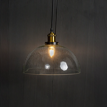 Clear glass dome pendant light glowing on black background with brass top and black fitting for stylish home decor.