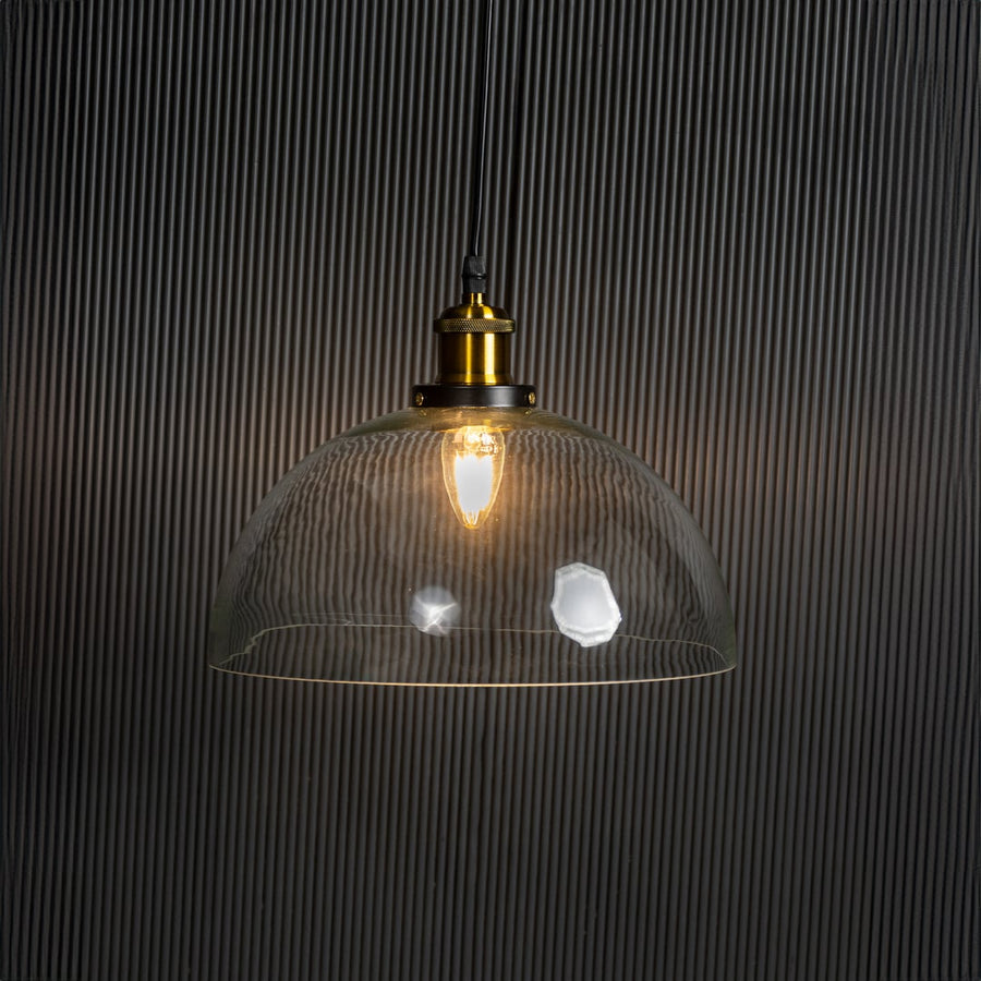 Clear glass dome pendant light glowing on black background with brass top and black fitting for stylish home decor.